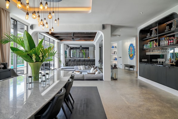 A modern kitchen with a large island, a dining area with chairs, and a bar area with shelves of bottles and glasses.