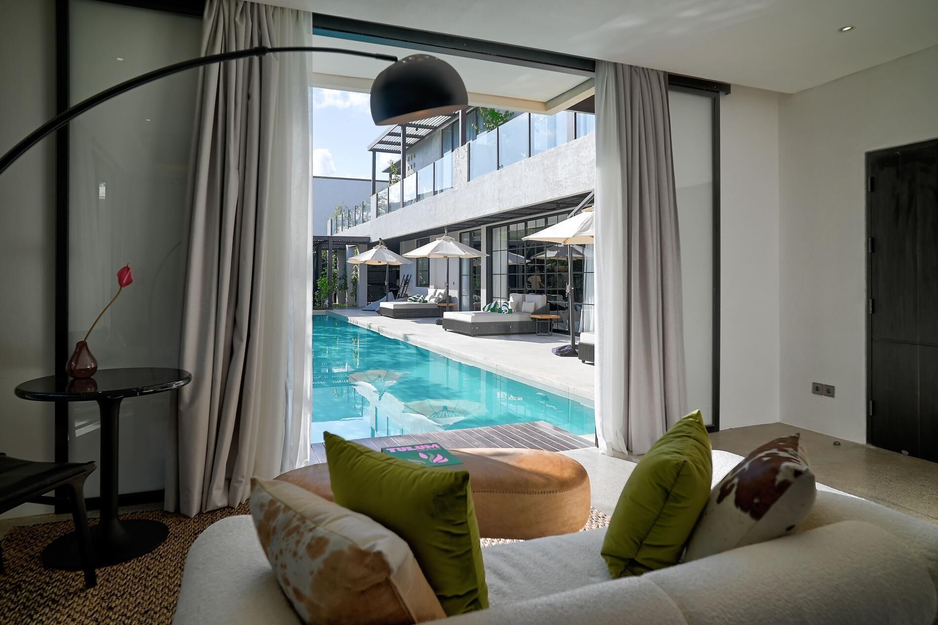 A modern hotel room with a large window overlooking a pool and outdoor seating area.