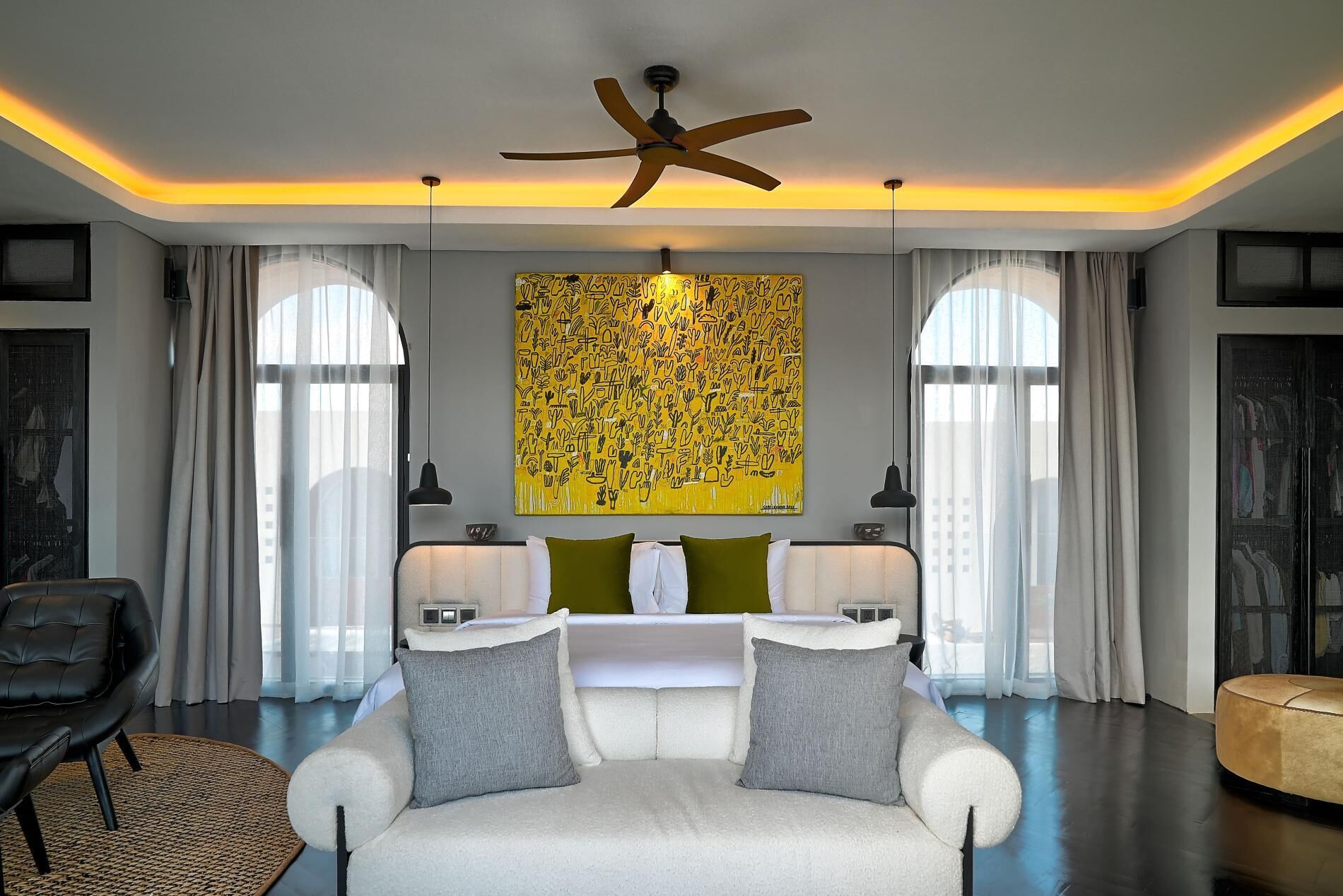 A modern living room with a white sofa, two green cushions, a ceiling fan, and a large abstract painting.