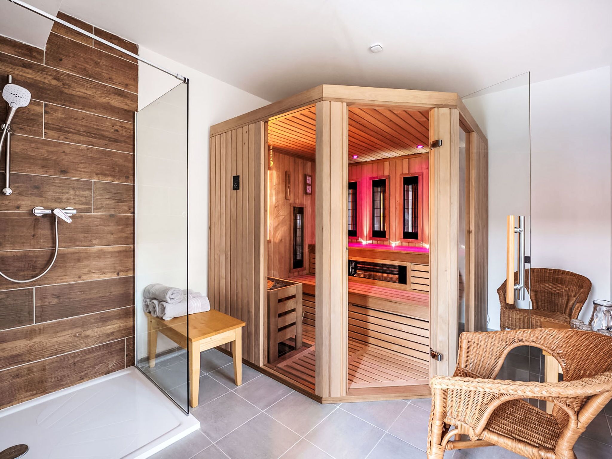 Een moderne badkamer met een houten sauna, een douchecabine van glas en een rieten stoel.
