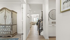 Un couloir avec une commode ancienne, un miroir et un escalier menant à une autre pièce.