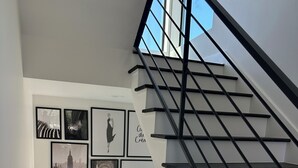 Un escalier moderne avec des rampes noires et une vue sur l’extérieur grâce à de grandes fenêtres.