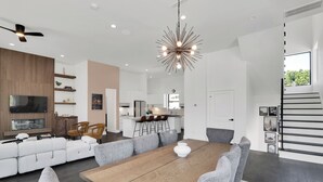 Un salon moderne avec une grande table à manger en bois, des canapés gris et un ventilateur de plafond.