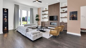 Un salon moderne avec un canapé d’angle, une table basse et un téléviseur. On y trouve également des étagères en bois et une plante.