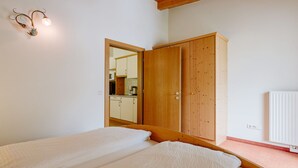 Habitación con dos camas, un armario de madera y un espejo que refleja la zona de la cocina.
