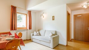 Una sala de estar acogedora con un sofá, una mesa de comedor con sillas, una ventana con cortinas y una puerta.