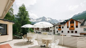 Una terraza con mesas al aire libre, sombrillas blancas y montañas al fondo.