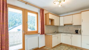 A kitchen with wooden cabinets, a countertop, a radiator, and a view of a forest through a window. - Apartment Nr. 7 by Interhome (Sulden)