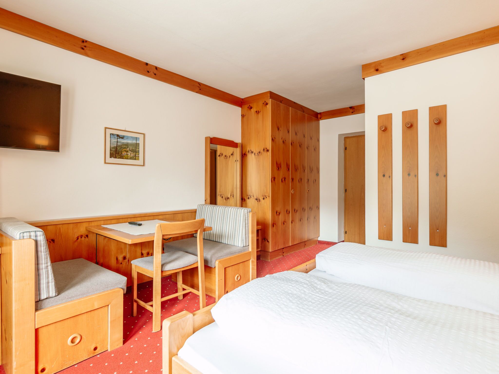 Een hotelkamer met een houten bed, een bureau met stoel, een aan de muur bevestigde televisie en een grote spiegel.