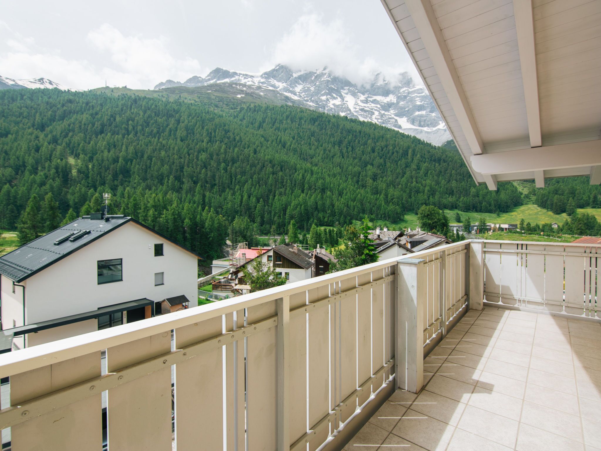 Un balcon donnant sur un paysage montagneux, un bâtiment doté d’un toit en pente et un ciel dégagé.