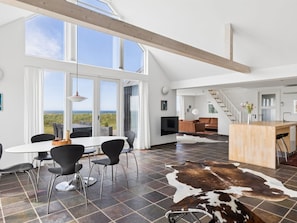 A spacious living area with a large window, a dining table, and a kitchen island.