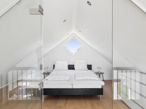Une chambre avec un plafond en pente, un lit avec une literie blanche, deux tables de chevet et un puits de lumière.