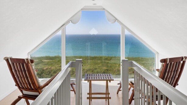 Un balcon avec vue sur l’océan, des chaises en bois et une table.