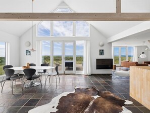 Un intérieur spacieux comprenant un coin repas, une cheminée et de grandes fenêtres offrant une vue sur l’extérieur.