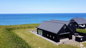 Un bâtiment moderne de couleur noire, doté d’un toit plat, de grandes fenêtres et offrant une vue sur la mer.