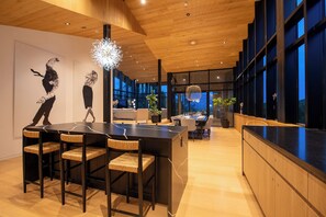 Cozinha moderna com ilha central, banquetas de bar e área de refeições com vista para a cidade.