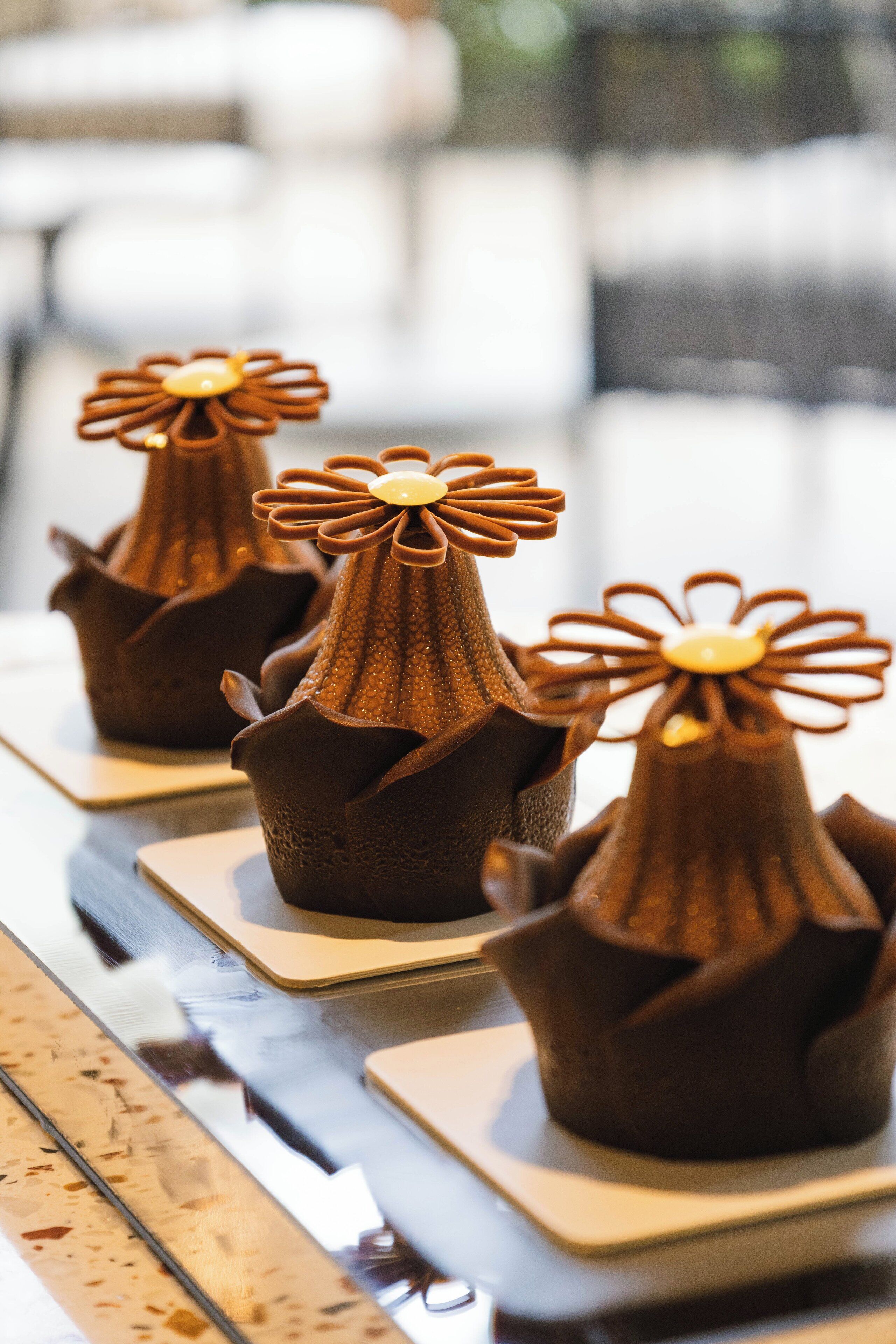 Una hilera de bombones con forma de flor, colocados sobre platos cuadrados.