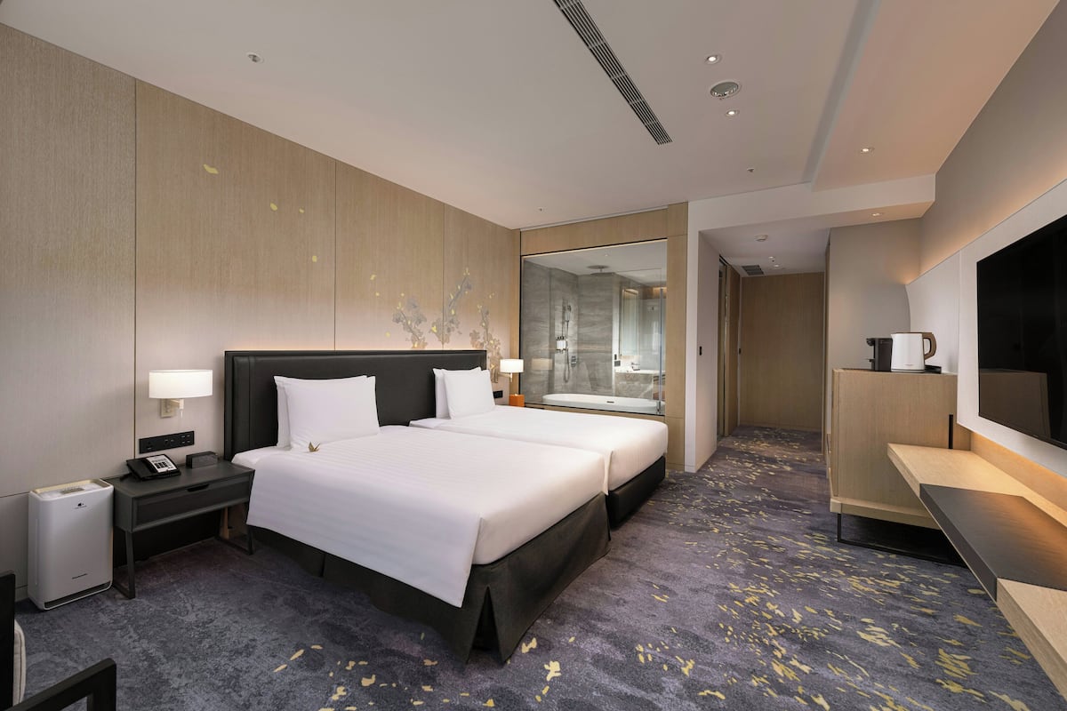 A hotel room with two beds, a desk, a mirror, and a TV.