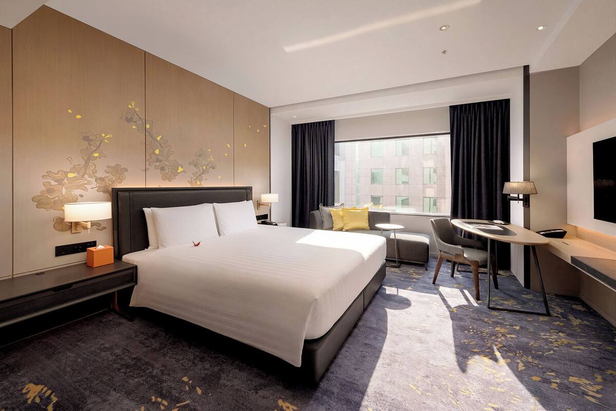 A hotel room with a large bed, a desk, a chair, a small table, and a window with curtains.