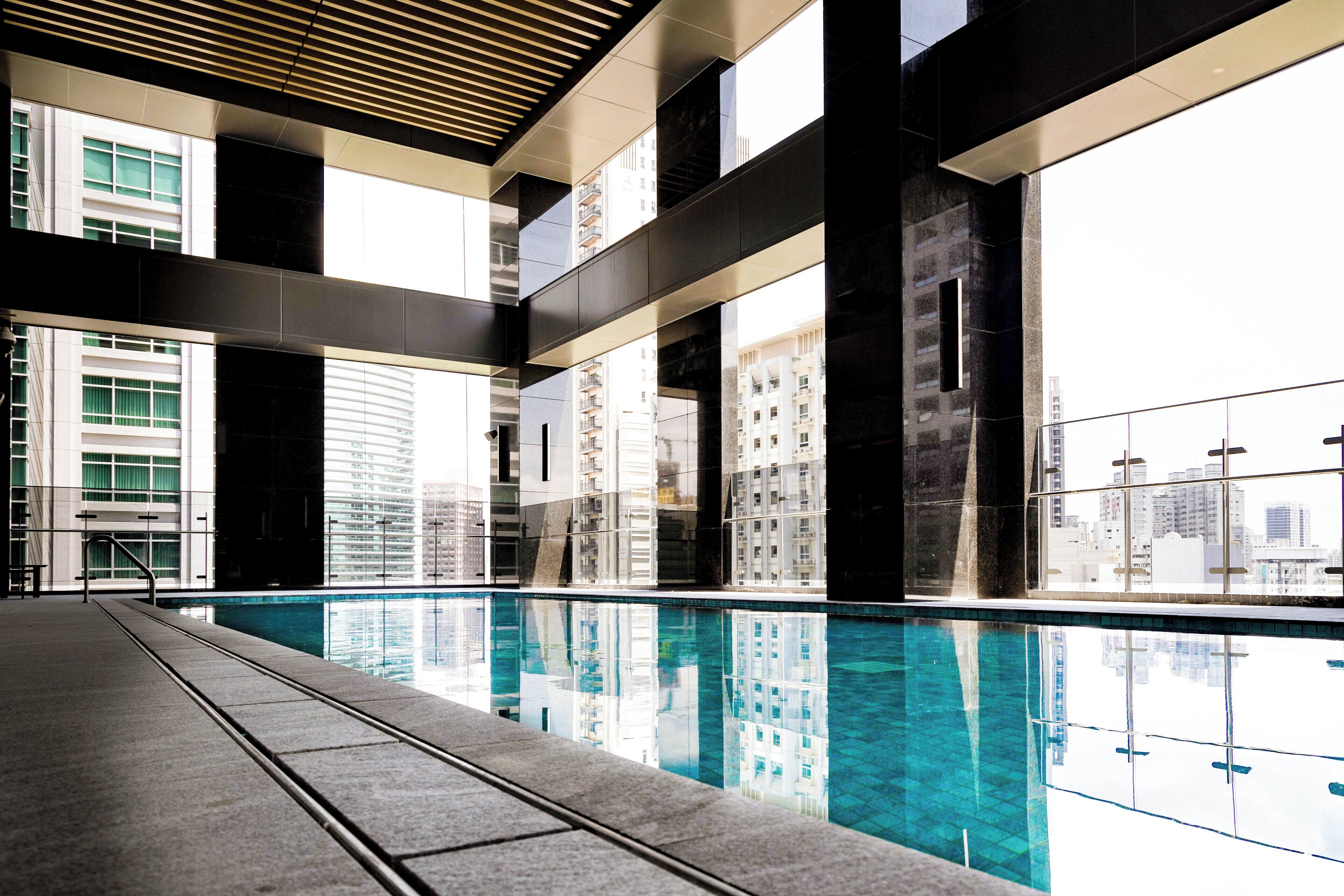 Una piscina interna moderna con riflessi chiari, ampie finestre e vista sugli edifici circostanti.