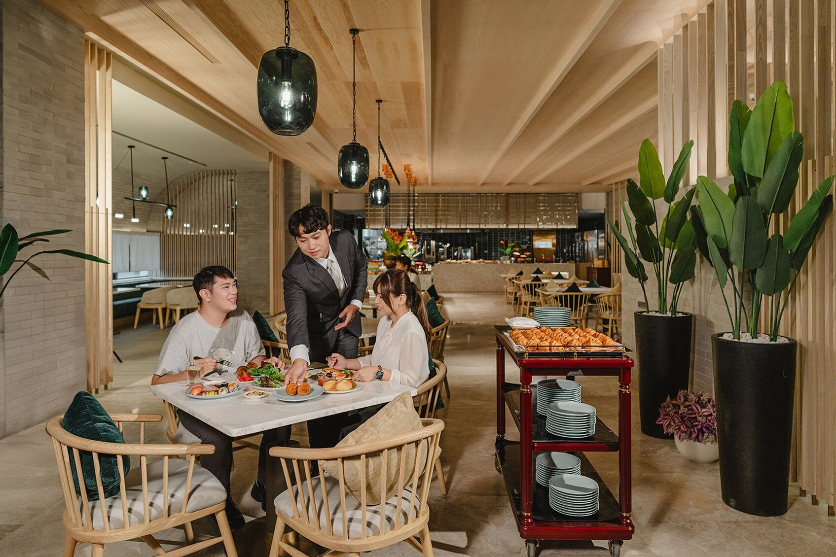 Un comedor moderno con mobiliario de madera, lámparas colgantes y una mesa de buffet con platos y pasteles.