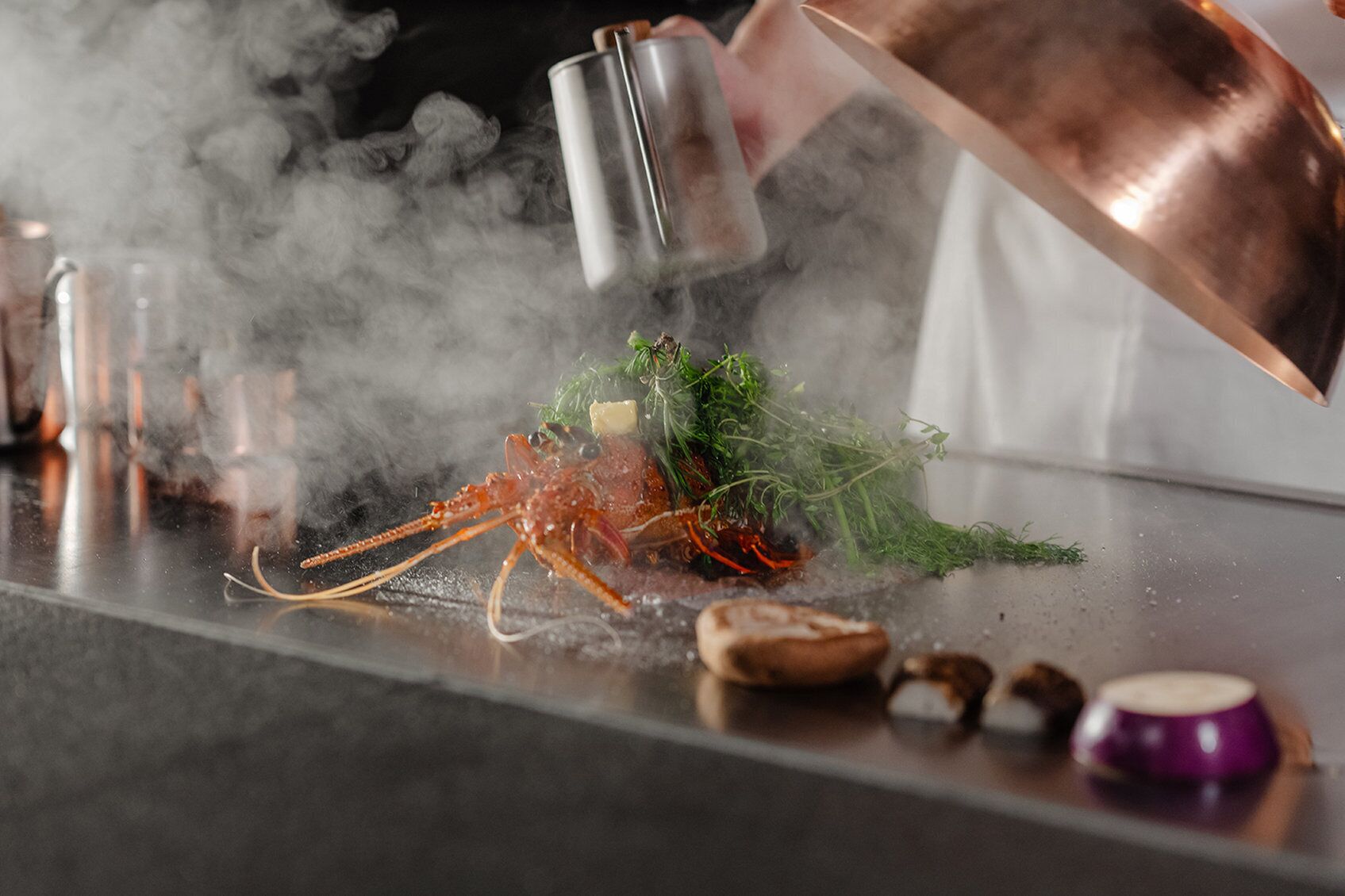 A lobster on a table with a copper pot and a metal shaker.