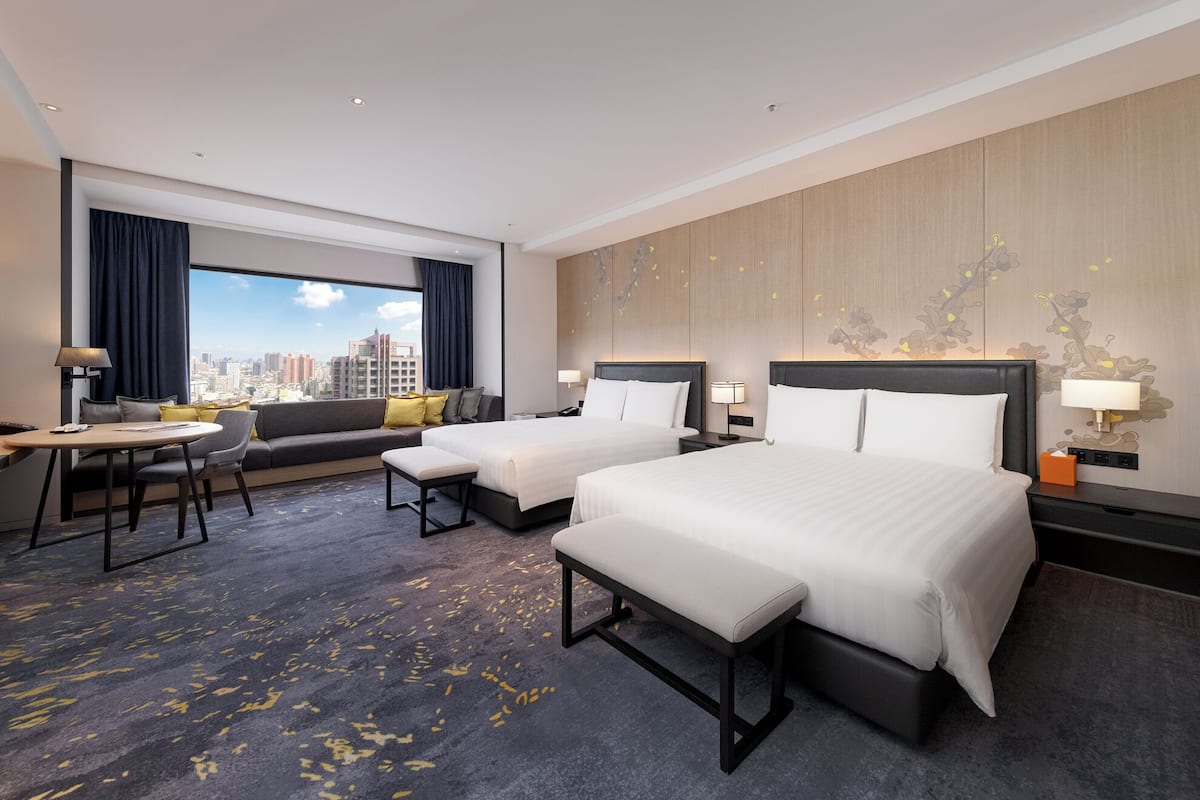 A hotel room with two beds, a sofa, a dining table, and a city view.