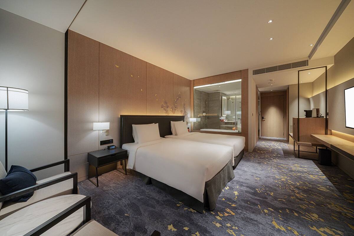 A modern hotel room with a large bed, bedside tables, a desk, and a mirror.