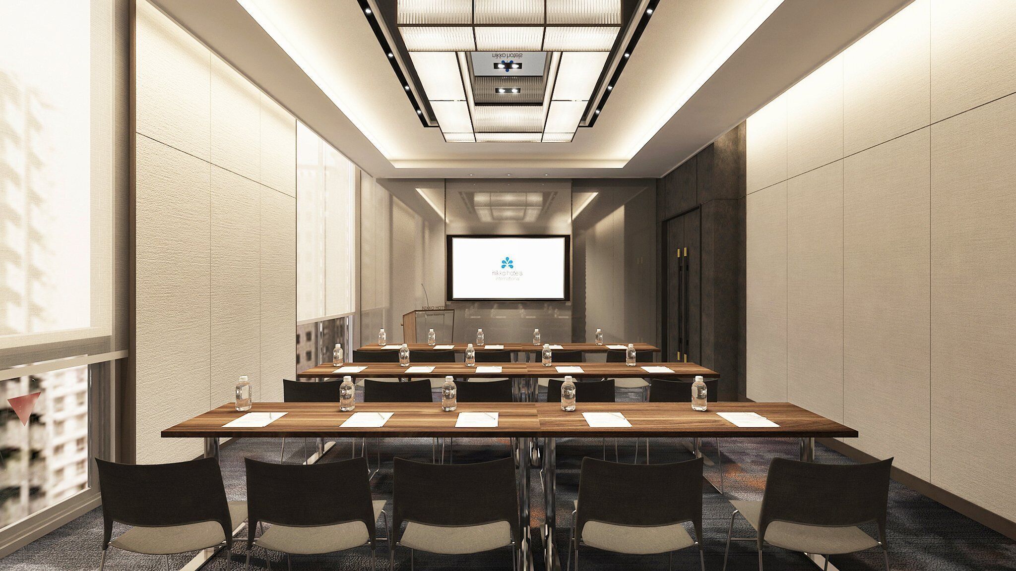 A conference room with a long table, chairs, a large screen, and a ceiling light fixture.