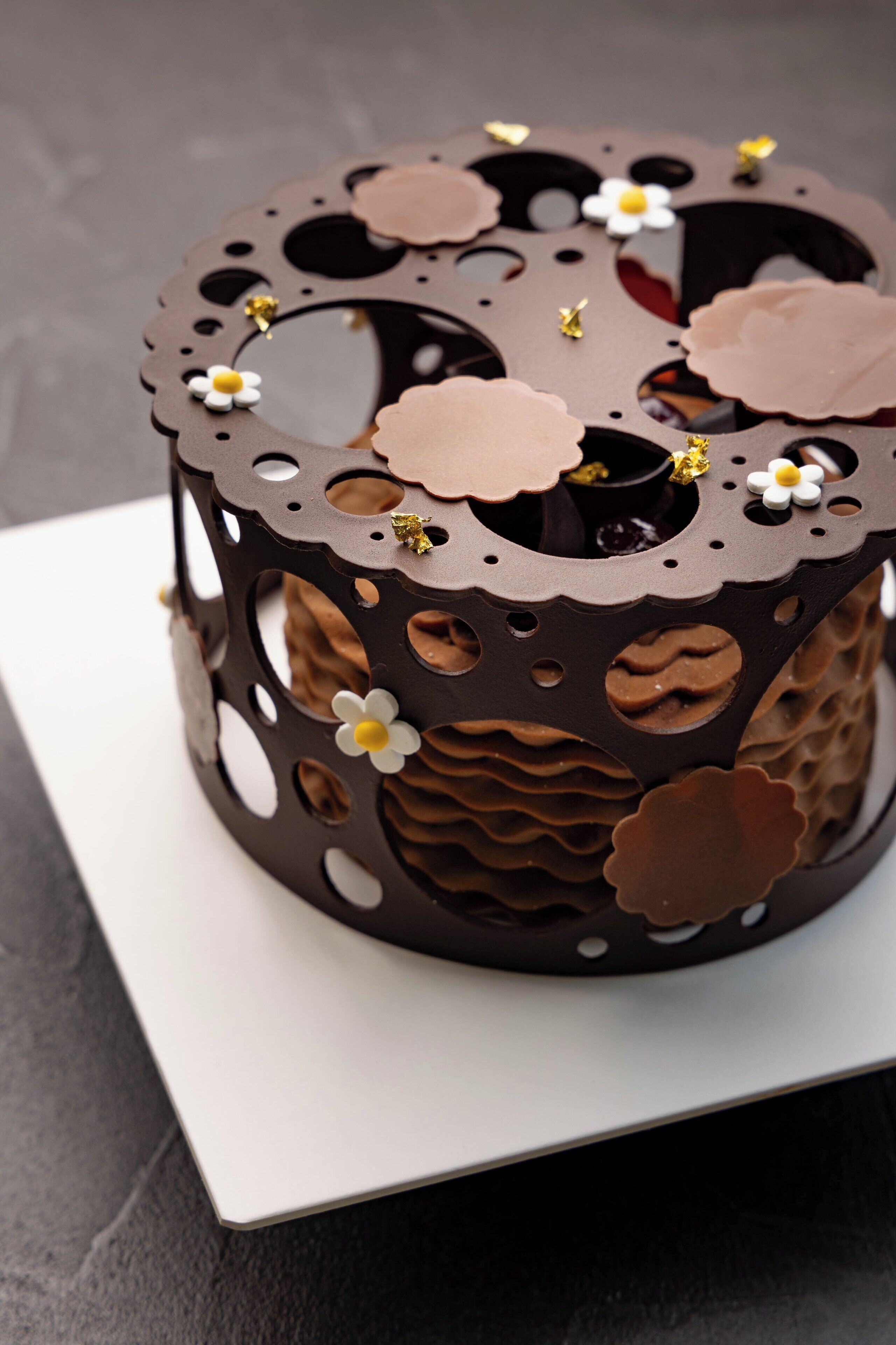 Un pastel de chocolate con diseños recortados y pequeñas flores en la parte superior.