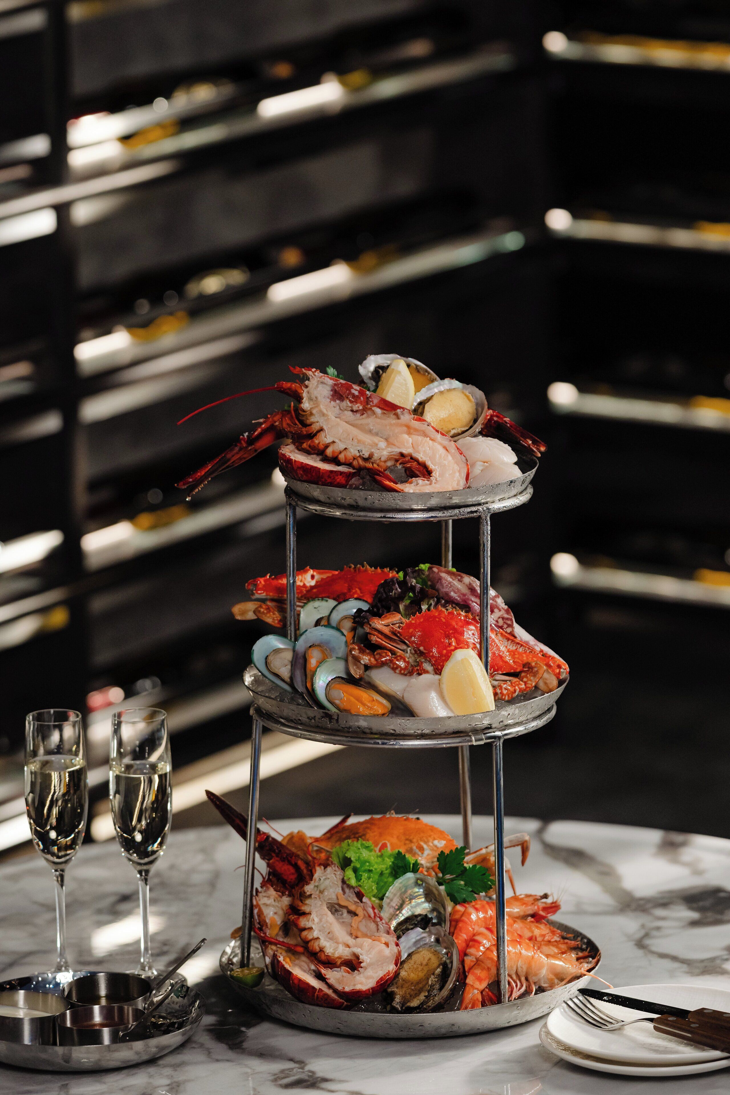 A seafood platter on a three-tiered stand with glasses and cutlery beside it.