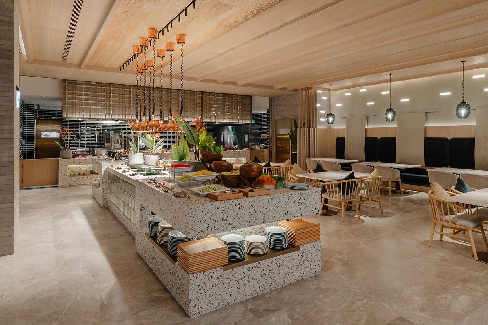 Una cucina moderna con isola centrale, zona pranzo con mobili in legno e illuminazione a sospensione.