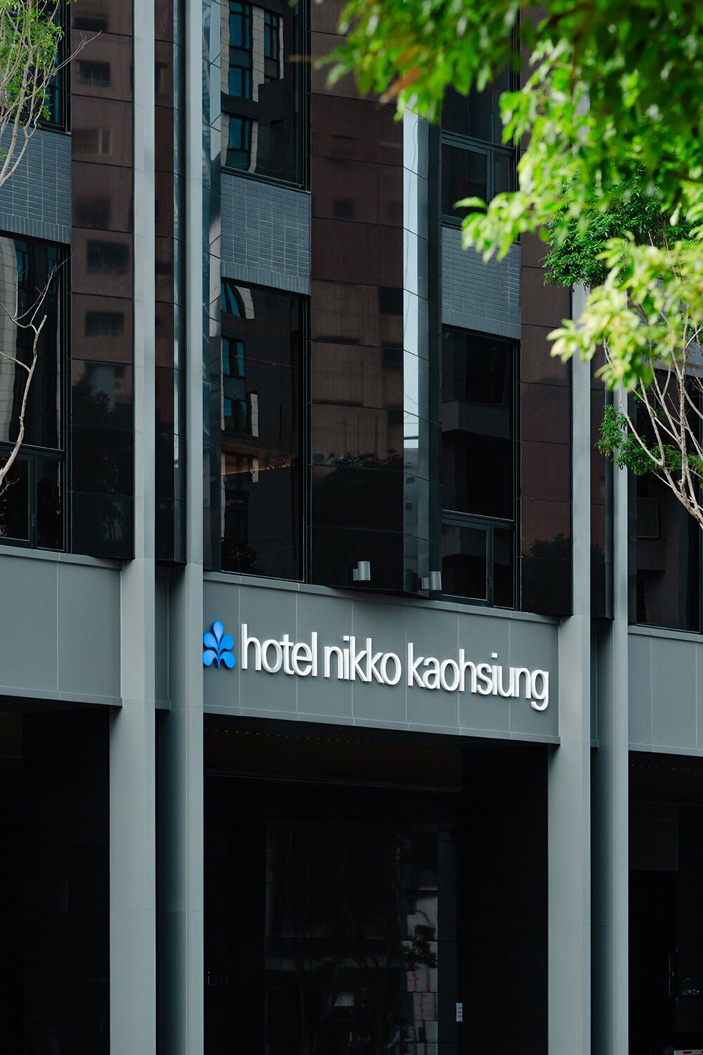 A hotel building with a modern facade, large windows, and a visible sign reading 'hotel nikko kaohsiung'.