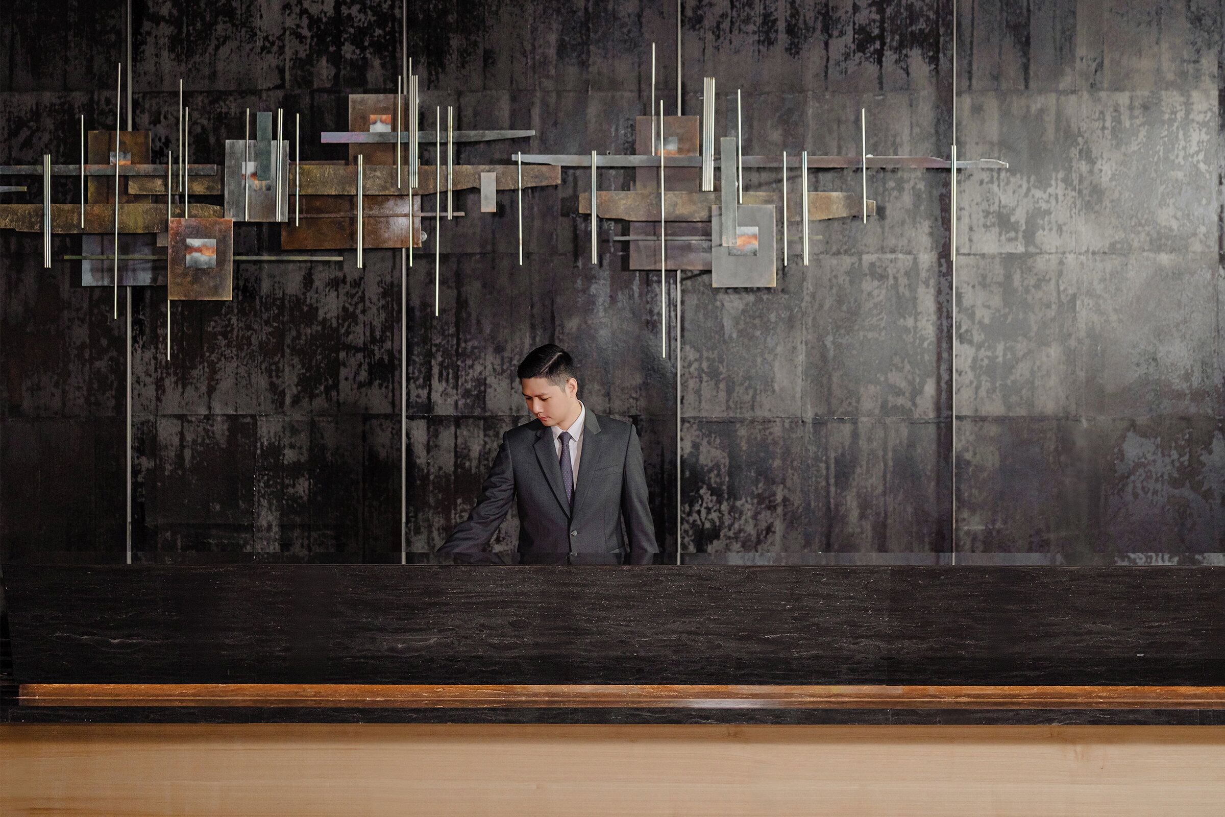 A man in a suit standing in front of a reception desk with a modern, industrial design.