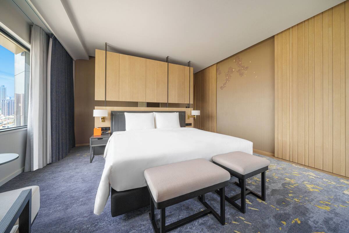 A modern hotel room with a large bed, a desk, and a view of the city.