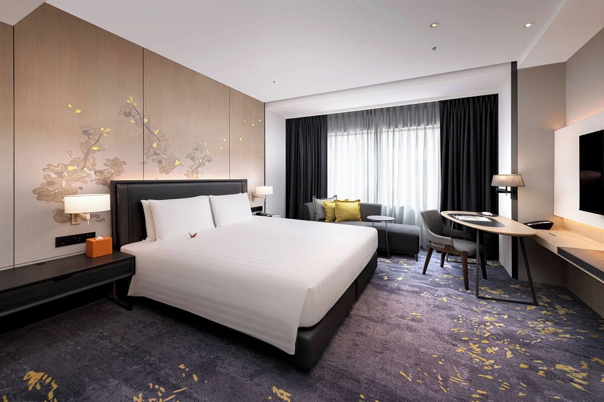 A hotel room with a large bed, a desk, a chair, a TV, and a window with curtains.