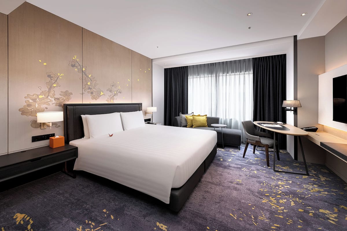 A hotel room with a large bed, a desk, a chair, a TV, and a window with curtains.