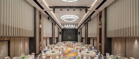 Un amplio salón de banquetes con mesas redondas, sillas blancas y un pasillo central decorado con arreglos florales.