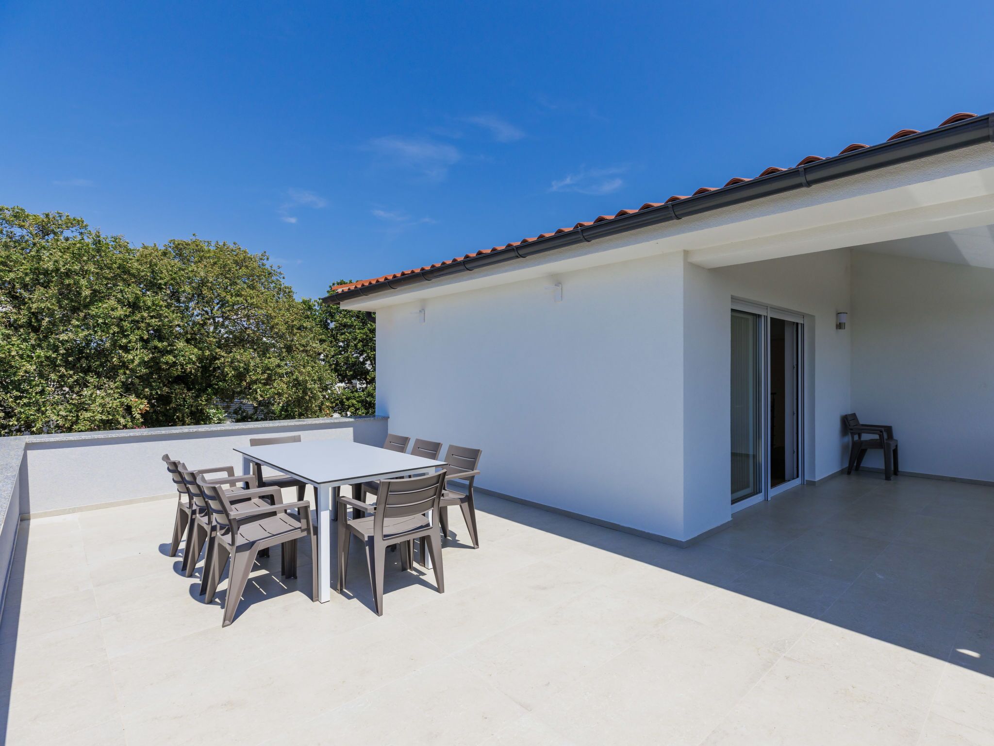 A covered patio with a table and chairs, a sliding glass door, and a view of trees.