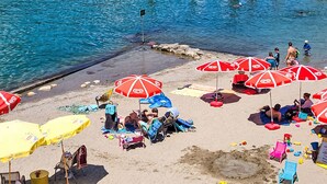 A beach with umbrellas, people relaxing, and a pier in the background.