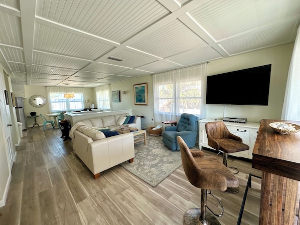 A spacious living area with a kitchen, a dining area, and a large TV.