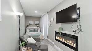 A modern hotel room with a flat-screen TV, a fireplace, a sofa, and a bed.