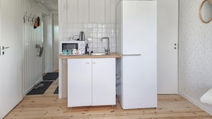 Una cocina compacta con armarios blancos, un microondas, un lavamanos y un refrigerador.