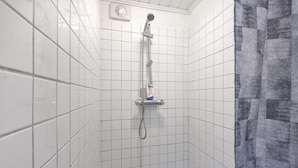 Ducha con azulejos, cabezal de ducha manual y una botella de champú en un estante.