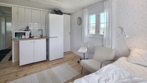 Una habitación compacta con kitchenette, una cama, una silla y un ventanal con cortinas.