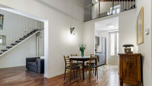 A spacious living area with a dining table, chairs, a sofa, a staircase, and a kitchen in the background. - GuestHost - Charming 80 sqm apartment, with mezzanine, for 6 people, located on the 4th floor of a renovated period building. The property is located in the heart of the historic center (Traffic-Restricted Area), between the lively Vucciria market and La (Palermo)