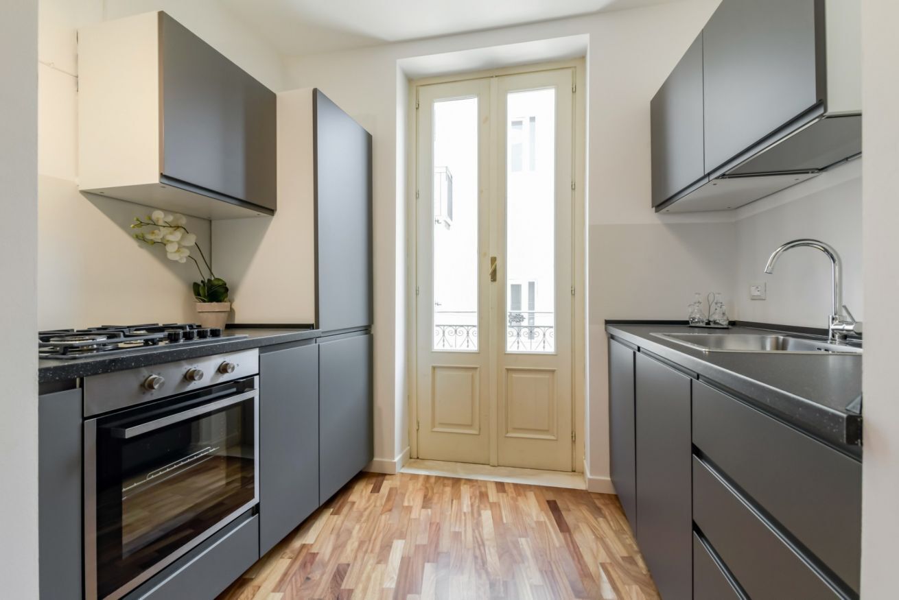 Una cocina moderna con estufa, horno y pileta, piso de madera, y una puerta que da a un balcón exterior.