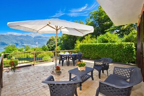 An outdoor patio with a table and chairs, a large umbrella, and a view of mountains.