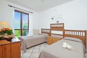 A bedroom with two beds, a wooden nightstand, a dresser, a window with curtains, and a wall with a decorative phrase.