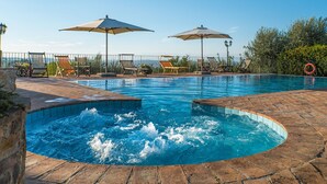 Une piscine avec un jacuzzi au centre, entourée de chaises longues et de parasols.